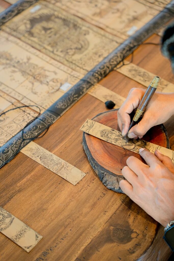 Hands etching a drawing onto a dried palm leaf during the Balinese Lontar Workshop at Paradisus by Meliá Bali