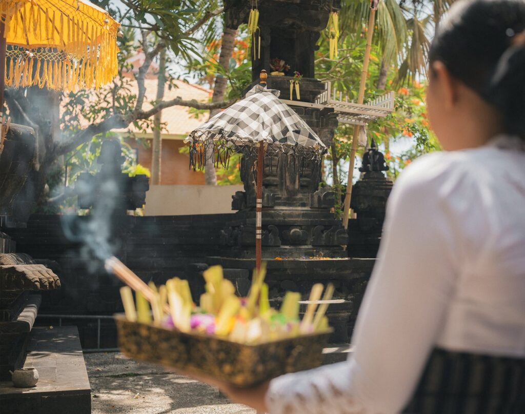 A team member in a white kebaya carrying a Balinese offering with incense to a shrine at one of the temples in the resort grounds at Paradisus by Meliá Bali